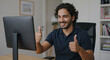 © Luiz - Man with curly hair giving thumbs up in front of a computer screen during a video call indoors