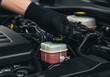 © Rubab - A gloved hand opening the brake fluid reservoir cap in a car engine compartment close up view