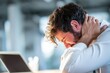 © ttonaorh - Unhappy businessman suffering from neck pain in the office, laptop on the desk, blurred background. Distressed man with his head between his hands and face down at the work table.