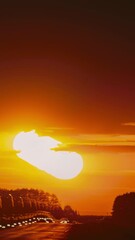 Wall Mural - Timelapse Big Sun Sundown Above Road Landscape. Dramatic Sunset Background. Road Trip Concept. Bewitching Illusion Of Car Silhouettes. Sunset Time Lapse, Time-lapse In Yellow, Orange Soft Colors