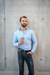 © Westend61 - Happy young businessman with disposable coffee cup standing in front of wall