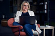 © Westend61 - Smiling businesswoman using laptop sitting on chair in office
