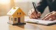 © Siti - Yellow Model House on Desk with Person Writing in Notebook in Bright Office