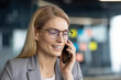 © Liubomir - A smiling businesswoman with blonde hair wears glasses while speaking on a cell phone, likely conducting business in an office setting.