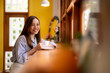 © Wasana - Smiling asian woman drinking coffee in cozy cafe
