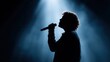 © SerPak - Silhouette of male singer with microphone in dramatic stage lighting.