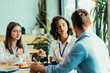 © Suteren Studio - Three young coworkers chatting over healthy lunch in bright office cafeteria