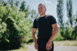 © qunica.com - A fit young man dressed in sportswear smiling in a lush green park setting. The sunny weather complements his active lifestyle, blending the essence of fitness and joy amidst nature.