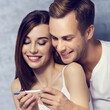 © vgstudio - Portrait of smiling amorous cute couple, looking at, finding out results on pregnancy test. Caucasian models - love, relationship, happy family concept, bricks wall background. Pregnant. Square