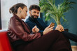 © qunica.com - A man and a woman conversing while looking at a smart phone. Features informal business attire, warm expressions, and a comfortable lounge environment with plants enhancing the ambiance.