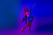 © deagreez - Young woman in casual denim fashion posing creatively under vibrant purple and blue neon light in studio