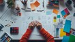 © Valentyna - Overhead view of a graphic designer's desk with hands working on sketches, surrounded by colorful stationery, digital tablet, and creative tools