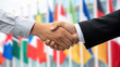 © n3wttfoto - Bilateral handshake between two business people with international flags in background symbolizing global trade and cooperation