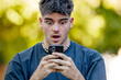 © carballo - young man in his 20s looking at his phone in surprise