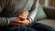 © Jittapon - Close up of a person sitting on a sofa holding their sto h in apparent pain or discomfort due to a gastro infection indigestion or constipation