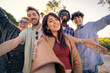 © Lomb - A happy young woman taking a selfie with her diverse friends outdoors. Point of view shot showing a multiethnic group celebrating friendship, community and togetherness.