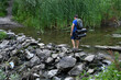 © Ольга Калинчук - A man crosses a river on rocks with a backpack.