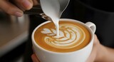 Pouring milk into a cup of coffee creating latte art with a leaf pattern in a white ceramic cup close up