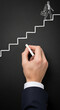 © Inspire Shots Hub - Chalk drawing of businessman ascending stairs on blackboard, hand holding chalk, depicting career progression and growth, showcasing potential and ambition
