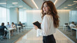 © NARUMOL - Professional woman in modern office setting, holding tablet and smiling confidently. background features colleagues engaged in discussions