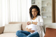 © Anastasiya - Black pregnant woman looking at smartwatch and breathing calmly, counting contractions. Represents birth preparation, and mindful focus during late pregnancy stage, copy space