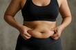 © Robbany Hossain - Woman pinching excess belly fat in workout clothes