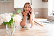 © Iryna - Woman talking on the phone in a bright kitchen while enjoying a cup of coffee and smiling warmly at the conversation