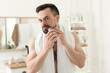 © New Africa - Handsome man shaving with trimmer in bathroom