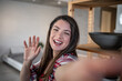 © Migma_Agency - Happy woman waving hand while making video call at home