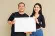 © Ranta Images - Portrait of young couple against plain wall background holding placard with copy space