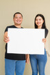 © Ranta Images - Portrait of young couple against plain wall background holding placard with copy space