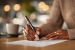 © whitestorm - Close-up of an African American woman signing paperwork with a pen at a table, accompanied by a cup of coffee, symbolizing business and commitment.