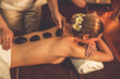 © InfiniteFlow - Hot stone massage at spa salon in luxury resort with warm candle light, blissful couple customer enjoying spa basalt stone massage glide over body with soothing warmth. Quiescent