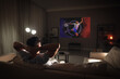 © New Africa - Man watching sports event using video projector on sofa at night