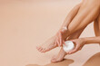 © st.kolesnikov - Woman Applying Foot Cream for Soft Skin and Wellness, Closeup of Skincare Routine on Neutral Background