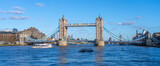 Tower Bridge stands majestically over the River Thames, showcasing its iconic architecture. A boat sails smoothly beneath the bridge on a bright and sunny day in London.