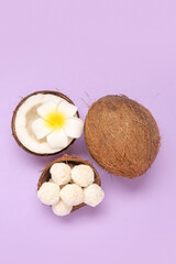 Wall Mural - Coconut shell with white chocolate candies and plumeria flower on lilac background