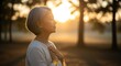 © kale.studio - serene elderly Asian woman with closed eyes and a peaceful expression places her hands over her heart, meditating or practicing mindfulness outdoors at sunset
