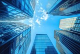 Looking up at several tall modern glass skyscrapers against a bright blue sky with scattered clouds, conveying a sense of urban scale and openness