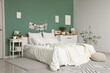 © Pixel-Shot - Interior of bedroom with big comfortable bed, pouf and chest of drawers near green wall