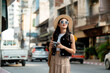 © Parichat - Young woman tourist exploring city street holding vintage camera