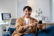 © Wasana - A man is sitting on a couch and pointing at his cell phone