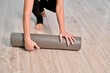 © TRAVELARIUM - Young woman rolling gray yoga mat on light wooden floor. Scene evokes calm and preparation in minimalist indoor setting, viewed from above