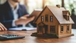 © Zakynanda - Wooden house model on desk, businessperson in background