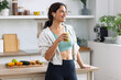 © nenetus - Kind sporty woman drinking a healthy green smoothie standing in the kitchen at home.