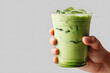 © Penkinn - hand holding glass of iced matcha latte against a plain background. Japanese green tea beverage for a cafe menu