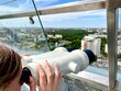 © Ina - Close-up view of young woman observing city panorama through a public binocular telescope on observation deck. Clear summer day. Minsk, Belarus.