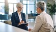 © Ayo - Two women in business attire, one writing in a notebook during a meeting