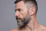 Man with short beard side profile close up, showing facial hair and serious expression on neutral gray background