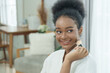 © Ekkasit A Siam - young african american teenage girl smiling while applying blush with makeup brush in white robe beauty care concept showing happiness skin health confidence selfcare lifestyle skincare moment